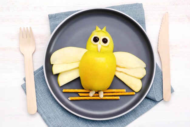 Funny owl face shape snack with apple wheat crispy bread straw on plate Cute kids childrens baby's sweet dessert healthy breakfastlunch food art on wooden backgroundtop view