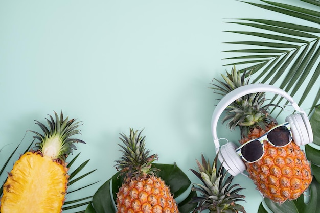 Funny pineapple wearing white headphone concept of listening music isolated on colored background with tropical palm leaves top view flat lay design