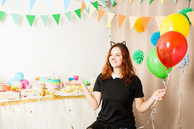 Funny playful girl animator in costume of cat holding colorful balls on the birthday party