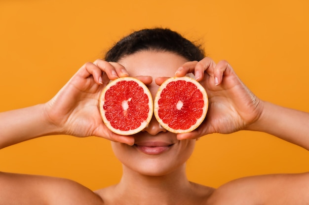 Funny playful young woman in checkered shirt holding halves of citrus fruits against her eyes