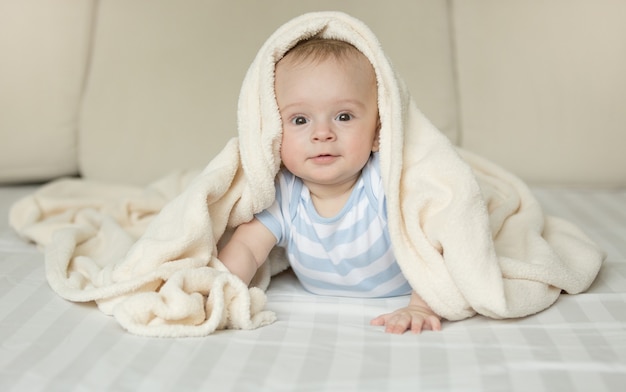 Funny portrait of baby boy looking at camera from under the blanket