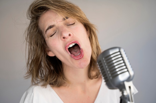 Funny portrait of caucasian woman singing a song with a vintage silver microphone.