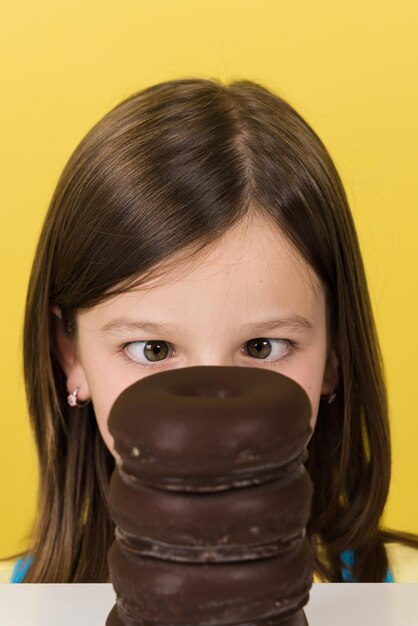 Funny portrait of little girl behind donut pile