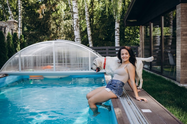 Funny portrait of smiling woman playing with dog and training golden retriever puppy in blue swimming pool Popular dog breeds outdoor activity and fun games with family pet on summer beach holiday