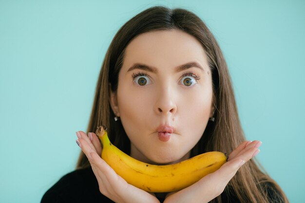 Funny portrait of young woman with banana on color background