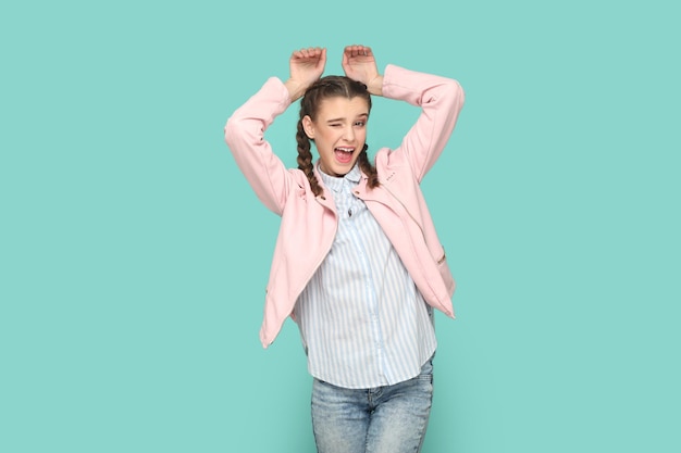 Funny positive childish teenager girl showing bunny ears winking to camera