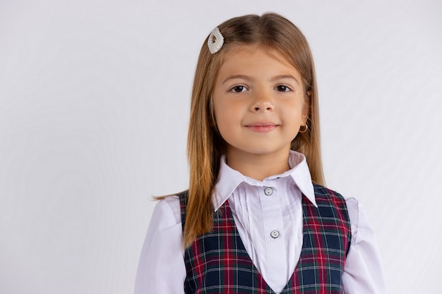 Funny positive kid primary school girl with long hair wearing uniform isolated on white wall. Happy caucasian child student close up headshot portrait.