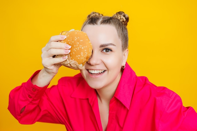 Foto divertente giovane donna incinta che mangia hamburger donna incinta che tiene gustoso panino mentre si trova isolato sul muro giallo dello studio concetto di cibo spazzatura fast food durante la gravidanza