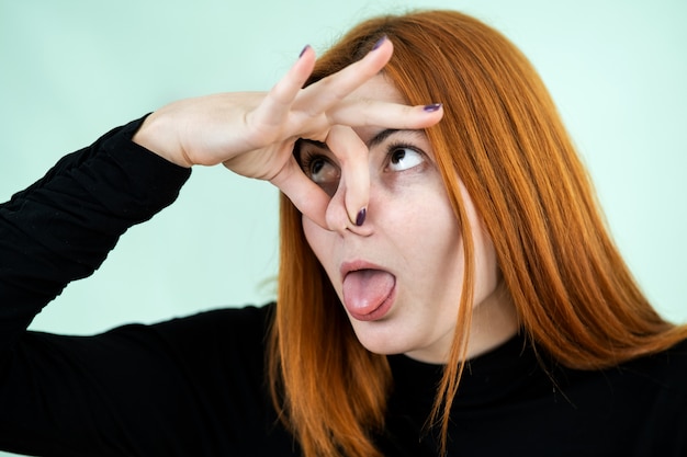 Photo funny pretty redhead girl showing bad smell sign with her fingers.