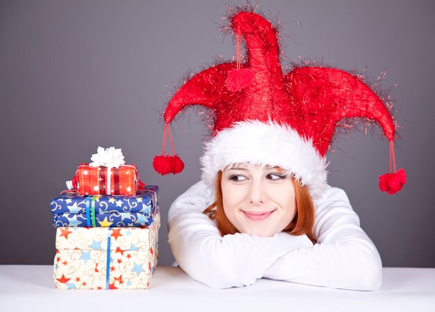 Смешная рыжеволосая девочка в рождественской шапке с подарочными коробками.