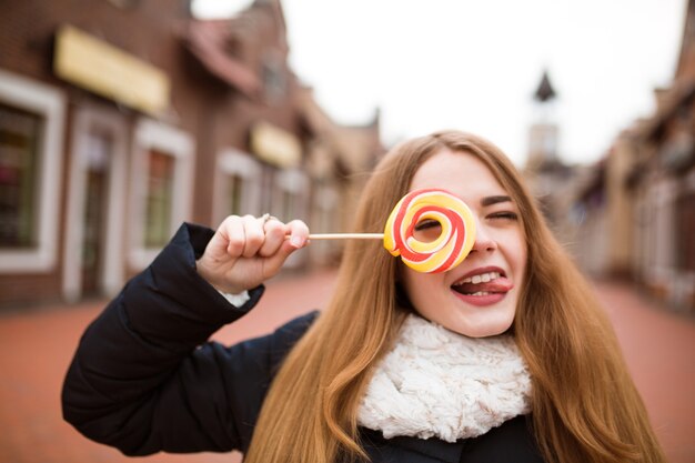 Divertente giovane donna dai capelli rossi che tiene in mano caramelle colorate di natale per la strada