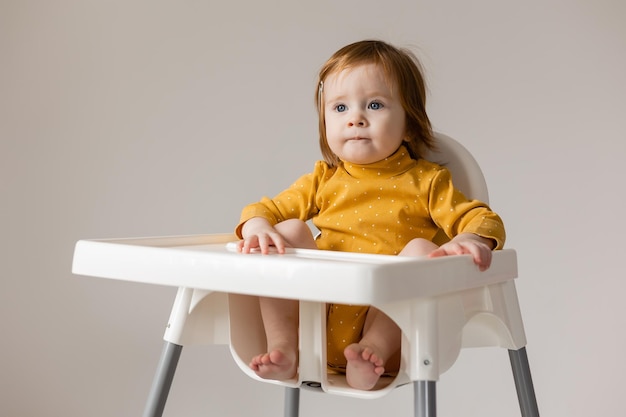 funny redhaired blueeyed baby in a yellow bodysuit sitting in a white high chair