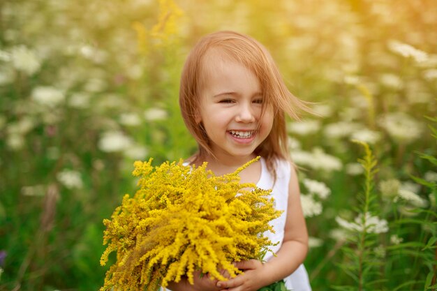 面白いredhaired女の子は黄色い花の花束でカメラを見て陽気に笑う