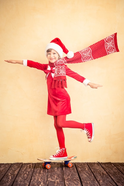 Funny Santa kid with flying scarf riding skateboard. Christmas holiday concept