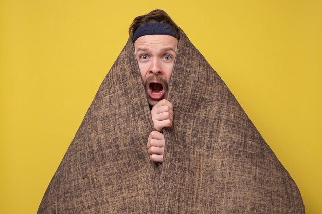 A funny scared man hides with a yoga mat