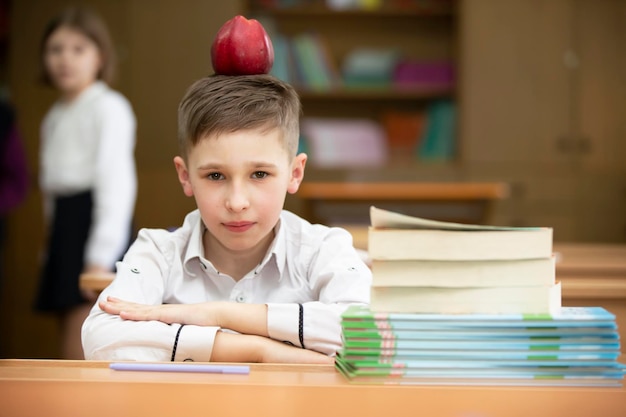 Funny schoolboy at the desk The boy in the class is playing around put an apple on his head