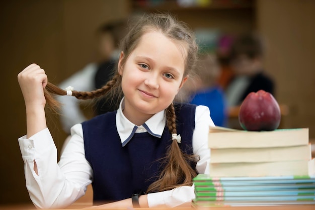 Funny schoolgirl with pigtails Girl in the classroom with books and an apple