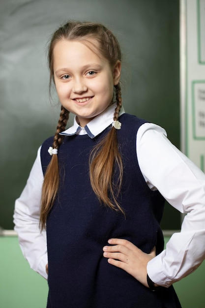 Photo funny schoolgirl with pigtails middle school age on the background of the blackboard