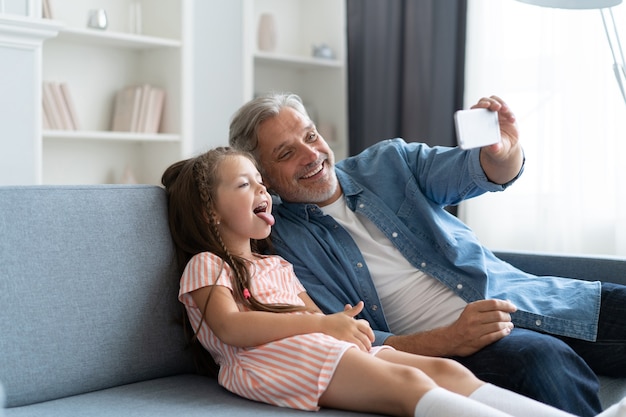 Funny selfie with dad. Self portrait of father and his little daughter taking selfie while sitting on the sofa.