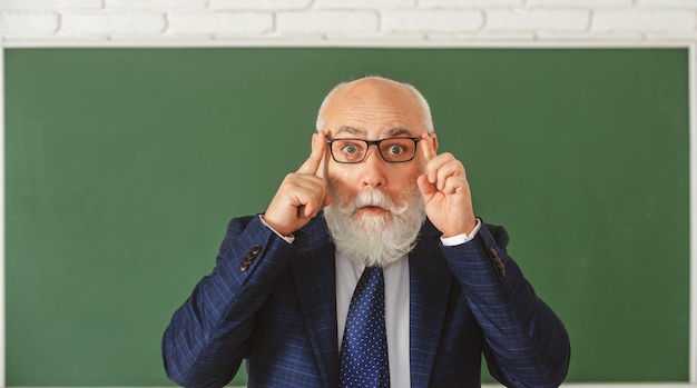 Funny senior professor in glasses surprised grey hair professor near blackboard think