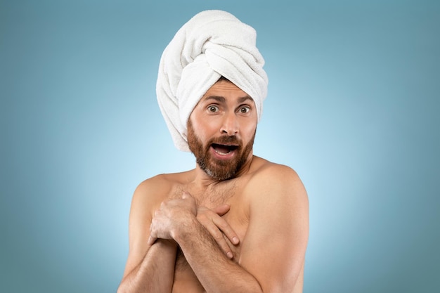 Funny shy man Handsome bearded guy with towel on head standing on blue background putting hands on his chest