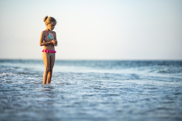 Funny slender cheerful girl playing with small waves, kicking their feet and spinning in place under the warm bright summer sun enjoying the long-awaited vacation