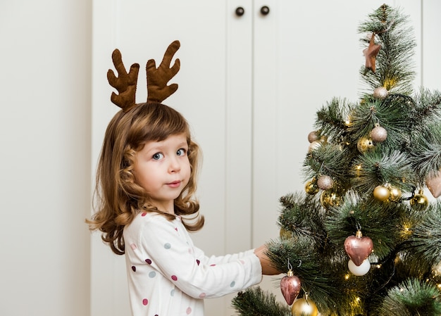 飾られたクリスマスツリーと面白い小さな女の子。白い背景。ミニマリストスタイル。