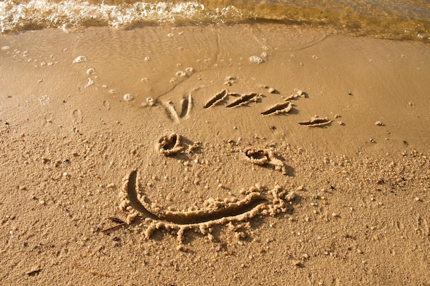 Foto una faccia sorridente disegnata sulla sabbia bagnata vicino al mare