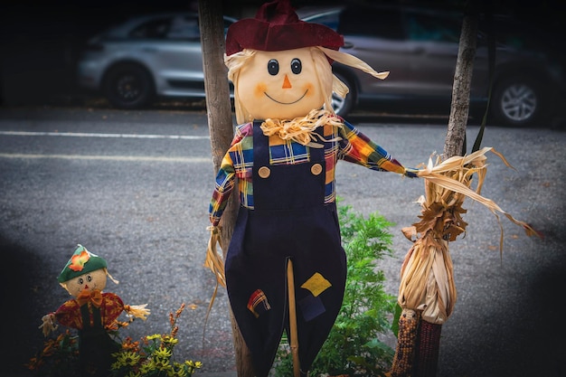 Photo funny and smiley scarecrow with corn on a wooden pole along a street in a city