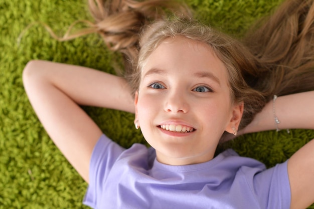 Смешная улыбающаяся маленькая девочка лежит на зеленом ковре