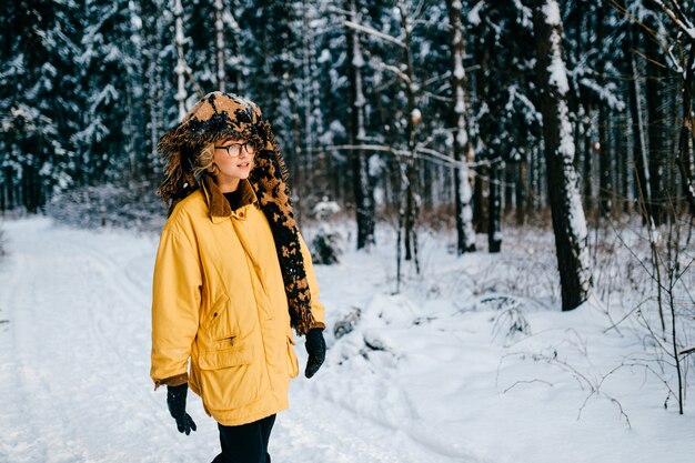 Funny strange young hipster girl with glasses and the scarf covering the head walking in the snow forest