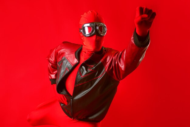 A funny super hero in a red leotard and protective glasses flying forward