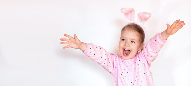 Funny surprise smiling child girl in pink blouse with Easter bunny ears opening her arms, copy space