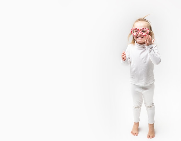 Foto bambina sorpresa divertente in bicchieri di caramello distoglie lo sguardo su sfondo bianco. copia spazio per il testo