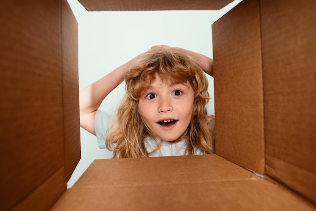 Funny surprised shocked child boy is opening gift and looking inside cardboard box kid opening packa