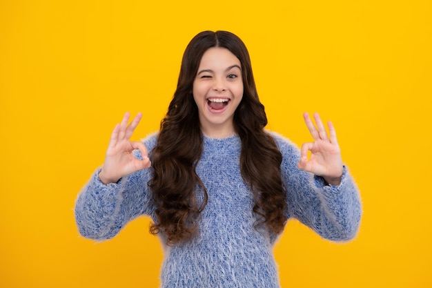 Divertente bambino adolescente su sfondo giallo facendo un gesto ok e ammiccando con la mano sorridente con la faccia felice adolescente stupito ragazza adolescente eccitata