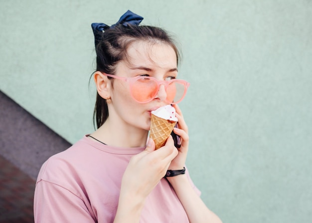 アイスクリームコーンを食べるクールな流行に敏感なサングラスの面白い十代の少女。夏の食べ物