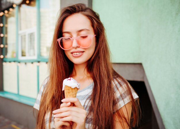 アイスクリームコーンを食べるクールな流行に敏感なサングラスの面白い十代の少女。夏の食べ物