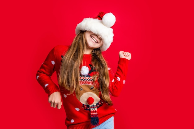 Funny teen girl dancing in santa claus hat on red christmas background christmas teen girl