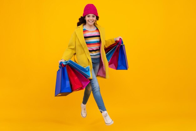 Funny teen girl hold shopping bag enjoying sale isolated on\
yellow portrait of teenager schoolgirl is ready to go shopping\
autumn shopping sale