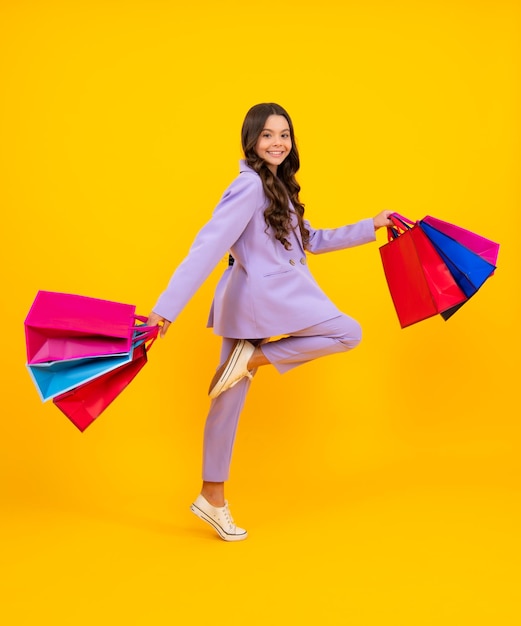 Funny teen girl hold shopping bag enjoying sale isolated on yellow Run and jump Portrait of teenager schoolgirl is ready to go shopping