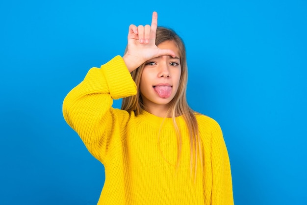 Funny teen girl makes loser gesture mocking at someone sticks out tongue making grimace face