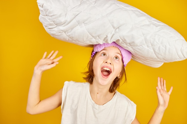 Funny teenage girl in white pyjamas with a violet sleeping mask hold pillow