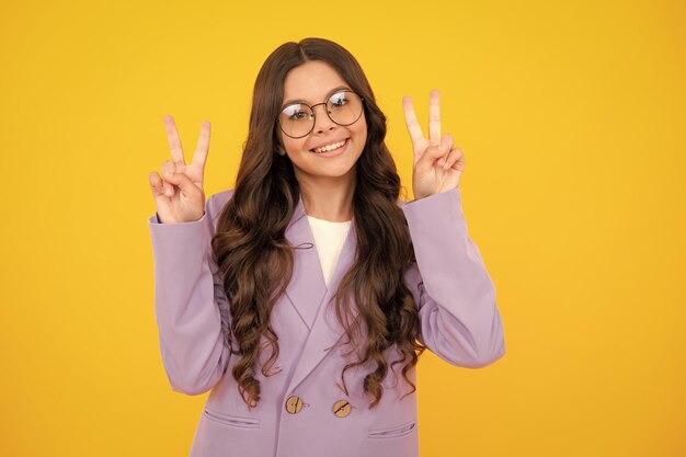 Funny teenager child girl show peace cool vsign isolated over yellow background