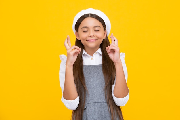 Photo funny teenager child holding fingers crossed for good luck girl prays and hopes dreams come true isolated on yellow background