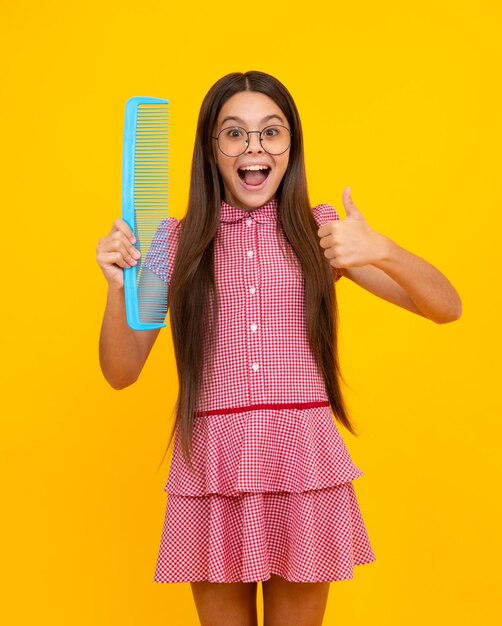 Funny teenager girl brushing hair with comb on yellow isolated studio background hairdresser