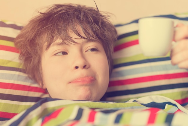 Funny teenager girl lying in bed with a cup of coffee in hand Toned