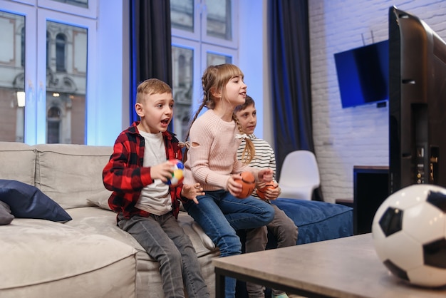 Funny three child friends are sitting on the couch at home and enjoying soccer match