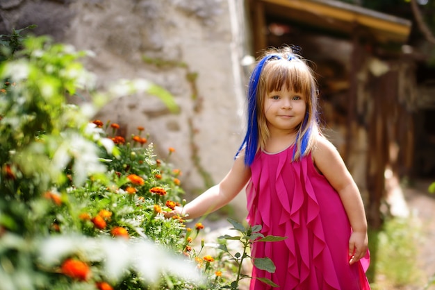 Funny toddler girl near the flowers next to the house