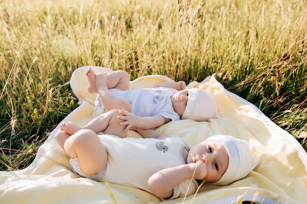 Funny twins sisters newborn babies lying on grass in summer day